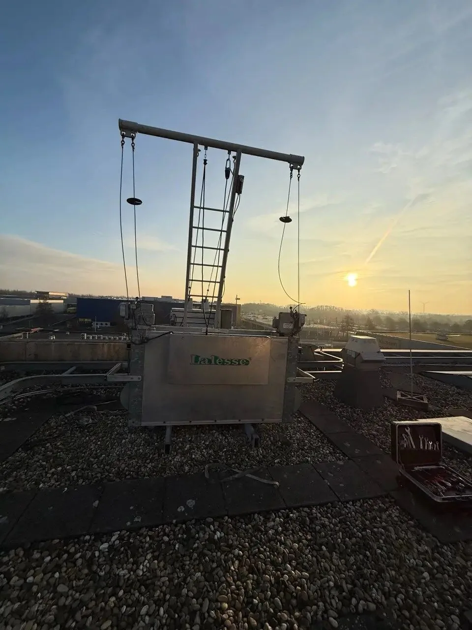 Gevelonderhoudsinstallatie met davit op een dak bij zonsondergang